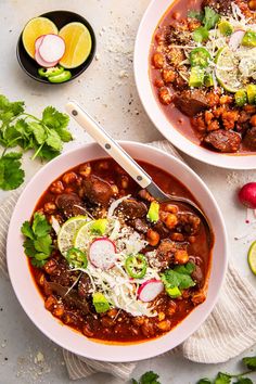 two bowls of chili and bean soup with cilantro, radishes, sour cream, lime wedges