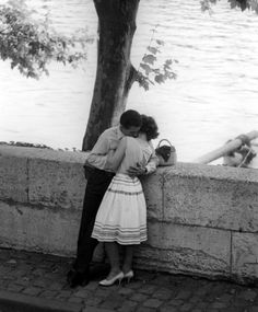 a man and woman leaning against a wall near the water