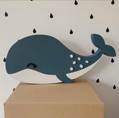 a wooden whale sculpture sitting on top of a cardboard box in front of a wall