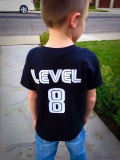 a young boy standing on the sidewalk wearing a level 8 shirt