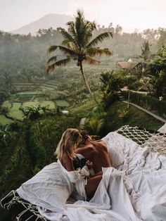 a woman laying in a hammock on top of a lush green hillside with palm trees