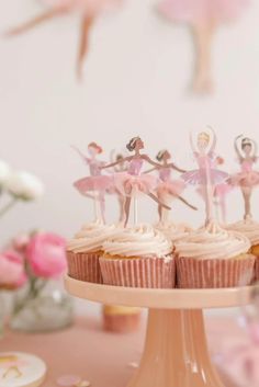 cupcakes with pink icing and little figurines on top are sitting on a cake stand