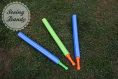 four plastic baseball bats laying on the grass with a sign saying seeing sandy in the background