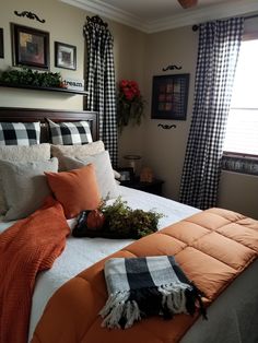 a bed with orange and black comforters in a bedroom next to a window filled with potted plants