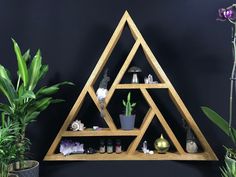 a wooden shelf with plants and rocks on it in the shape of a triangle, against a black wall