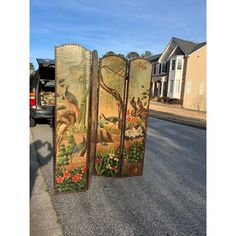 three painted screens sitting on the side of a road in front of a truck and house