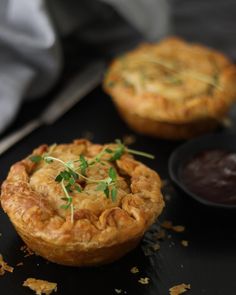 two small pies sitting on top of a black plate next to a bowl of sauce