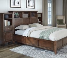 a bedroom with a bed, chair and bookcases on the floor in front of two windows