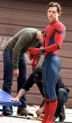 a man in a spider - man suit standing next to another man on a skateboard