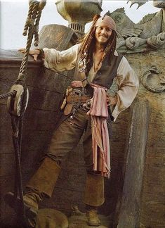 a man dressed as a pirate standing on the deck of a ship with his hands in his pockets