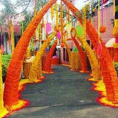 an archway decorated with orange and yellow flowers in the middle of a street lined with trees