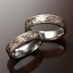 two silver wedding bands with engraved designs on the sides, set against a dark background