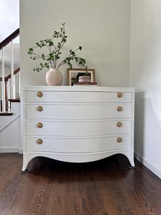 a white dresser sitting in the corner of a room with a plant on top of it