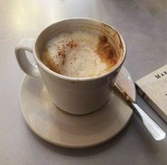 a cup of cappuccino sits on a saucer next to a book