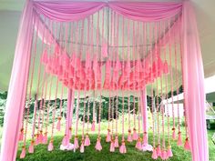 a pink and white canopy with tassels hanging from it's sides in the grass