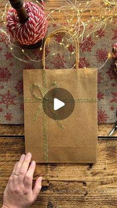 someone holding a brown paper bag with a bow on it and yarn in the background