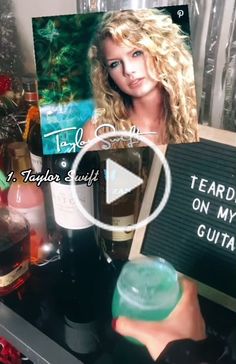 a woman holding a bottle of wine in front of a sign that says teardrop on my guitar