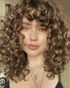 a close up of a person with curly hair and green eyes wearing a black top