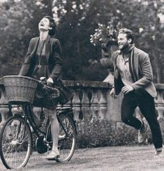 a man and woman are riding bicycles in the park while one looks up at the sky