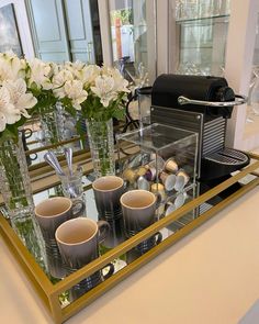 there are cups and vases on the counter in front of the coffee maker, which is also filled with flowers