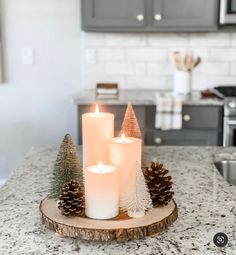 three lit candles sitting on top of a wooden plate next to pine cones and fir trees