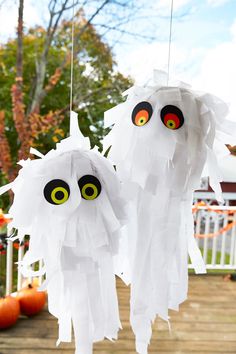 two paper ghost decorations hanging from strings on a porch with pumpkins and trees in the background