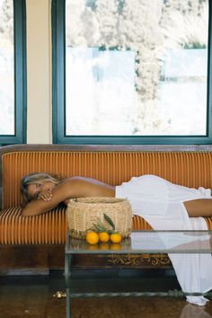 a woman laying on top of a couch next to a table with oranges in it