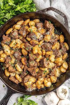 an iron skillet filled with meat and garlic on top of a marble countertop