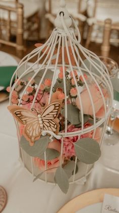 a birdcage filled with lots of flowers on top of a white table cloth