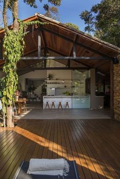 an outdoor kitchen and dining area with wood flooring on the outside wall, surrounded by greenery