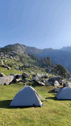 two tents set up on the side of a mountain with grass and rocks in the foreground