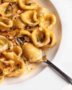 a white plate topped with pasta covered in sauce and onions next to a fork on top of a table