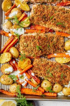 baked fish and vegetables on a baking sheet with lemon wedges, parmesan cheese, carrots, potatoes