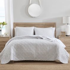 a bed with white and grey striped comforter in a bedroom next to a window