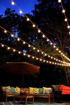 an outdoor seating area with lights strung over it and a patio table in the foreground