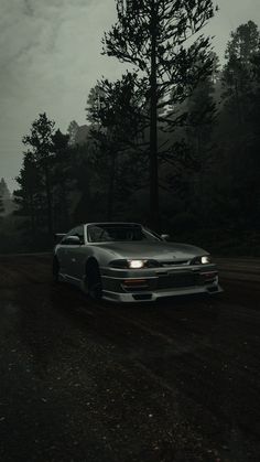 a car parked on the side of a dirt road in front of some tall trees