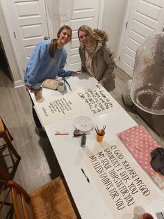 two women sitting at a table with writing on it