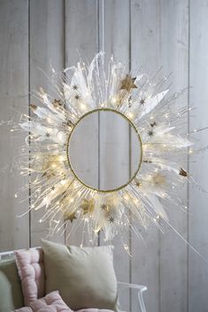 a white wreath with gold stars hanging from the ceiling next to a chair and pillows