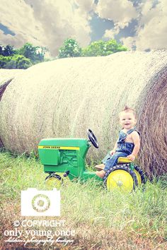 a little boy sitting on top of a tractor next to a hay bail in the grass