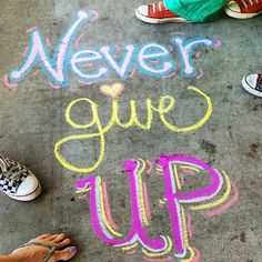 someone is standing on the sidewalk with their feet in front of chalk writing that says never give up