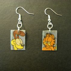 These earrings are made from a Garfield comic strip by Jim Davis, from a Sunday newspaper. They feature Garfield on one, and Odie on the other. On the back of the Odie earring is part of the word 'BARK!'; on the back of the Garfield earring, Garfield is splashing coffee in his face, after Odie barked at him! The comic clippings are attached to rectangular pieces of plastic bread bag clips, and have been coated with several layers of finish to protect them and give them a glossy look. The ear hooks and jump rings are silver plated.  The earring panels (not including the rings and hooks) are about 13/16 of an inch high by 9/16 of an inch wide. They are water-resistant, but may not be water-proof, so wearing them in the pool, shower, etc. is not recommended. This is a re-purposed item made fr Garfield Jewelry, Garfield Earrings, Garfield Comic, Garfield Images, Bottle Cap Earrings, Garfield Cartoon, Recycled Earrings, Garfield Cat, Garfield Comics