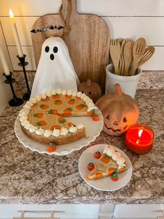 a table topped with a cake covered in frosting next to a pumpkin and ghost