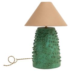 a green table lamp with a beige shade on it and a cord attached to the base