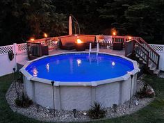 an above ground swimming pool with lights on the deck and fire pit in the middle