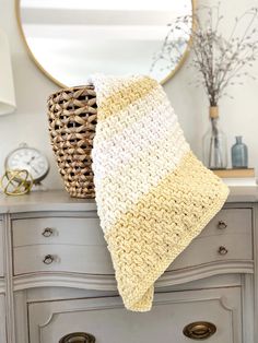 a white and yellow crocheted blanket sitting on top of a dresser next to a mirror