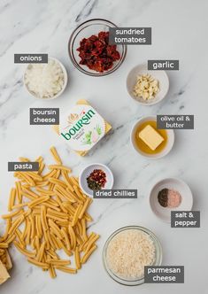 the ingredients to make pasta laid out on a white marble counter top, including parmesan cheese, sundried tomatoes, garlic and other ingredients