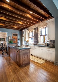 an open kitchen and living room with hardwood floors, exposed beams, and white cabinets