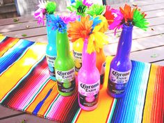 three bottles with flowers in them sitting on a colorful table cloth next to each other