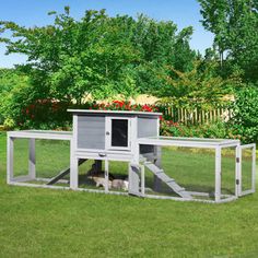 a chicken coop in the middle of a grassy field with flowers and trees behind it