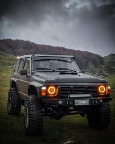 an off - road vehicle is parked on the grass in front of a hill with dark clouds